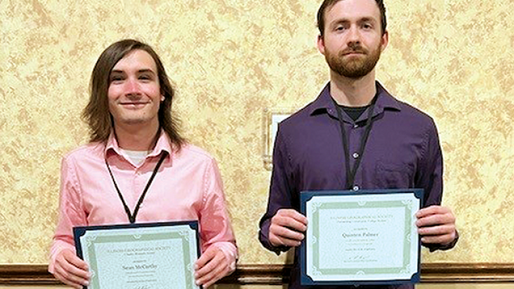 Two male students pose for a photo holding an award certificate.