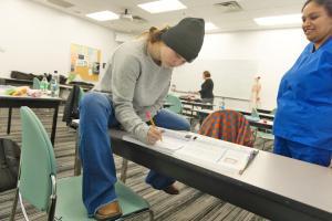A CNA student sitting on a table studying with peers.
